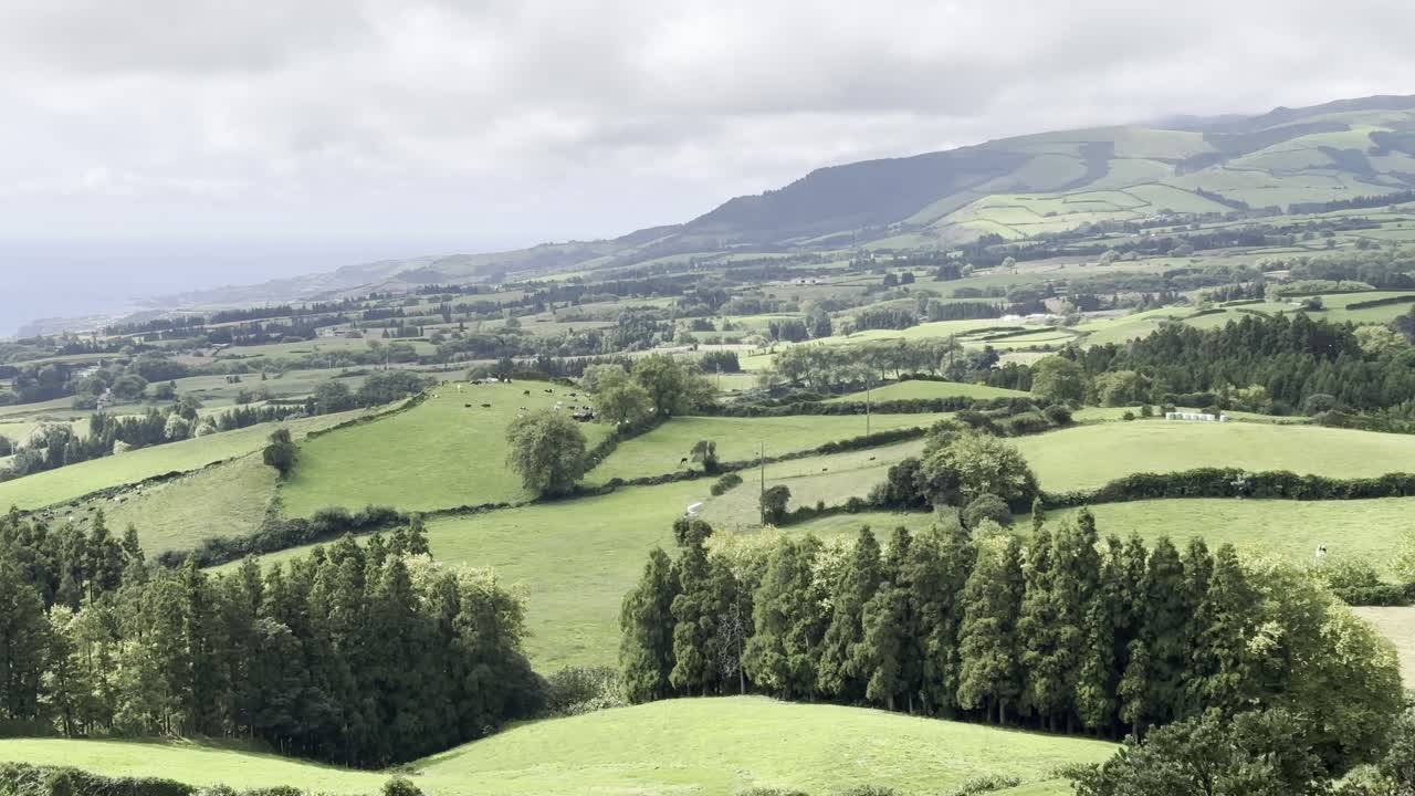 Wide view of São Miguel Island's lush green fields extending toward the ocean, set beneath a clear, cloudy sky