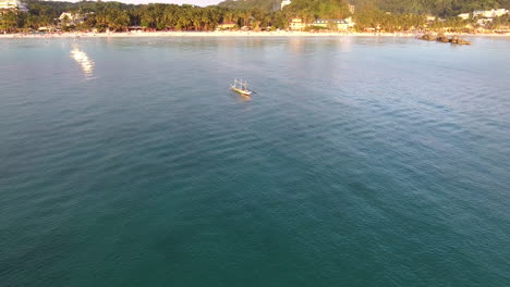 Aerial-shot-of-a-sailboat-passing-through-the-frame-with-the-shoreline-in-front-of-it