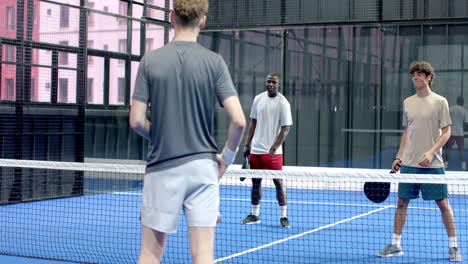 playing padel tennis, diverse group focusing on intense match on blue on indoor court