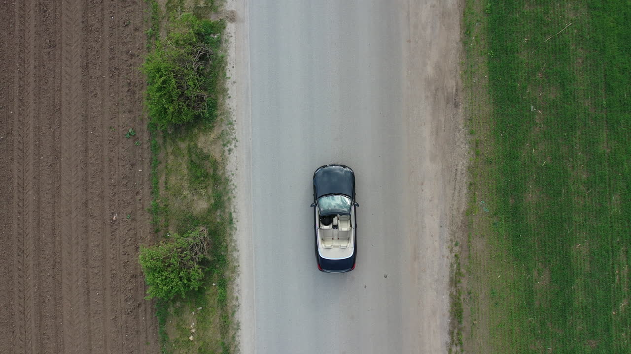 vista aérea a vista de pájaro del coche convertible y del conductor que se desplazan por la carretera rural