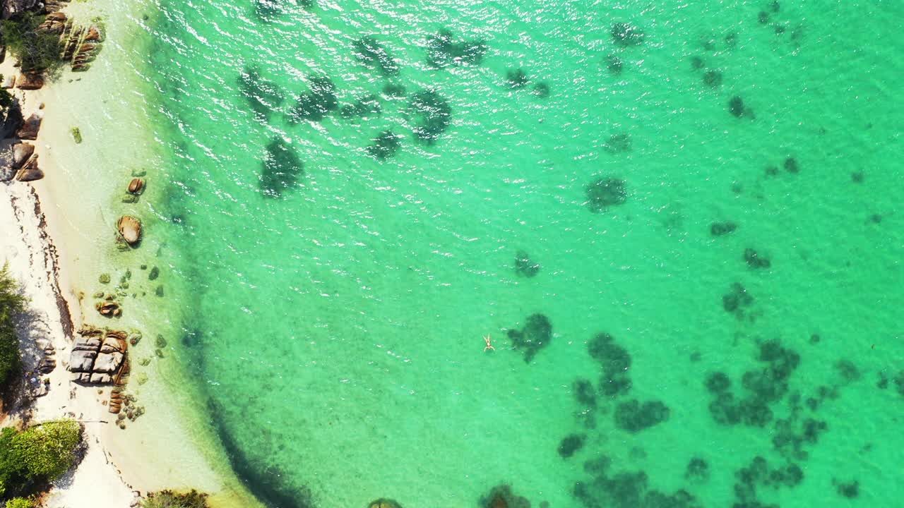 Beautiful Balinese azure sea water. Woman floating on the crystal clear sea. aerial shot revealing sandy beach with some boulders