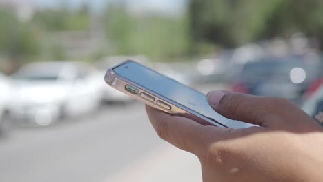 a person using a smartphone on a street with cars in the background