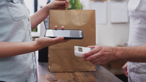 close up of woman in store making contactless payment at sales desk holding mobile phone to reader