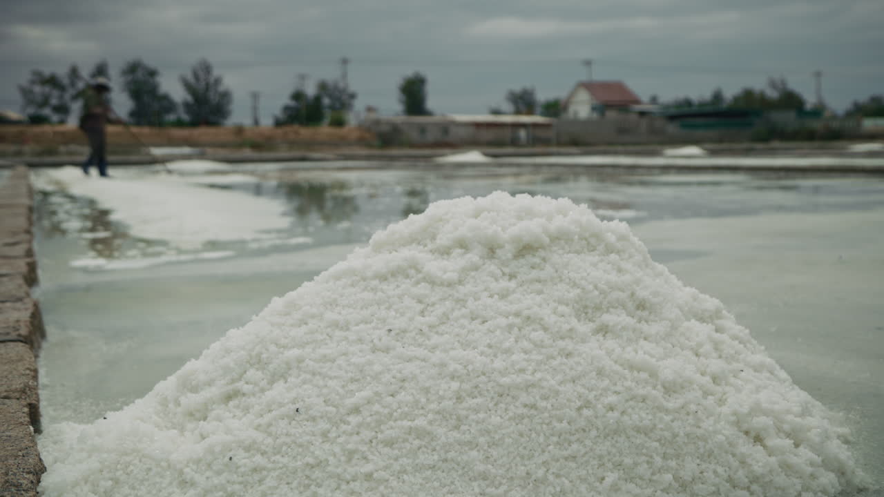 A large pile of salt in a salt pan with a worker in the background