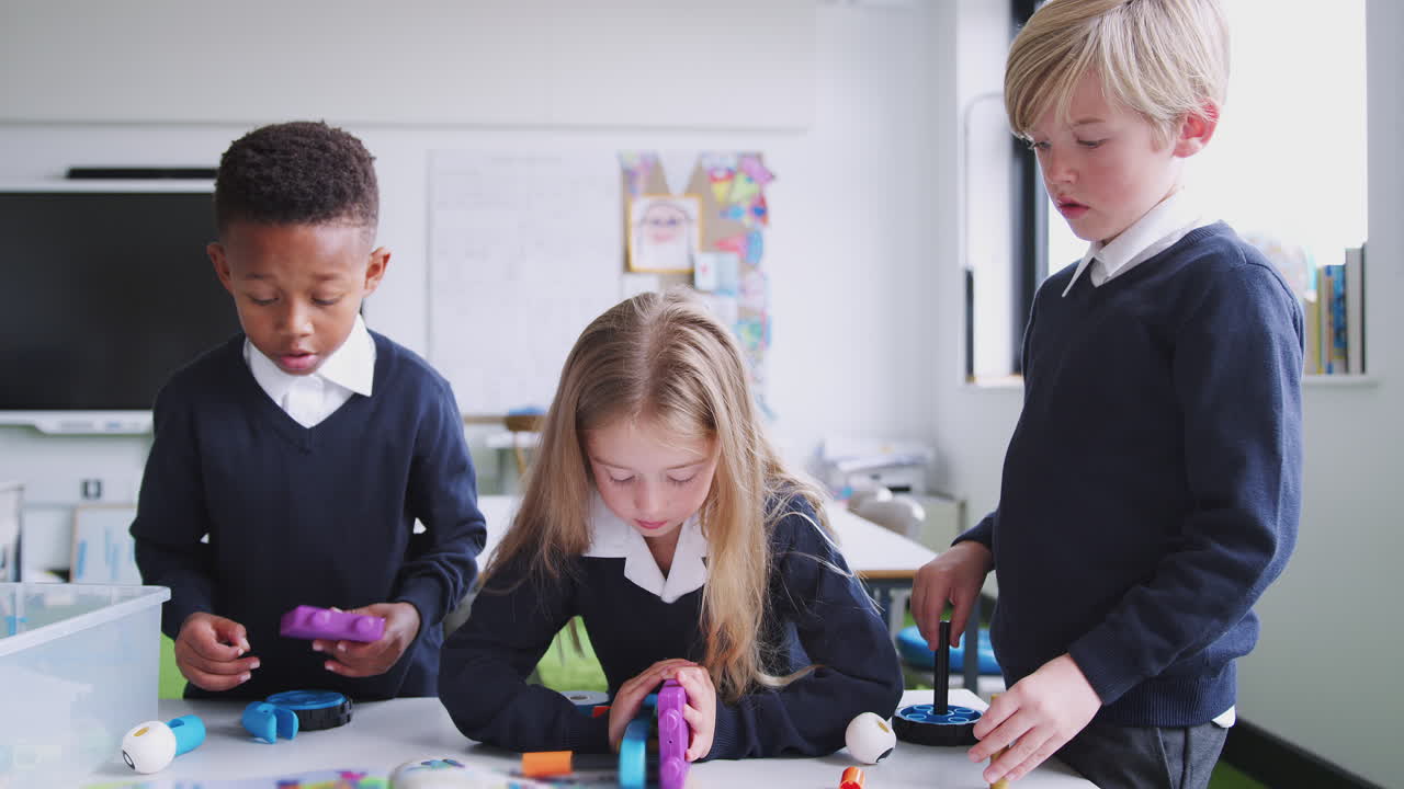 A girl and two boys working together with construction blocks in primary school classroom, close up