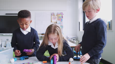 A-girl-and-two-boys-working-together-with-construction-blocks-in-primary-school-classroom,-close-up