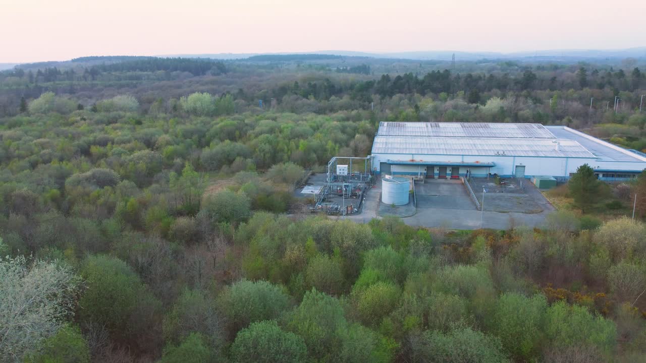 Drone Aerial View Over Warehouse with Loading Bays Surrounded by Forest Landscape. Industrial Infrastructre Surrounded by Natural Environment. 4K
