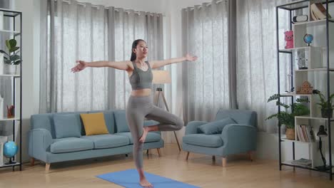 joven atlética asiática en ropa deportiva haciendo yoga en la postura del árbol en la alfombra en casa