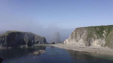 Aerial-retreat-from-eroded-sea-arches-in-rugged-grassy-coastal-islet