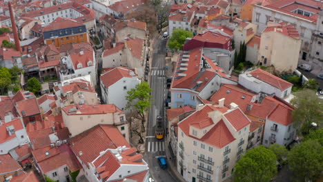 Aerial-overhead-top-down-view-of-yellow-tram-driving-on-the-tracks-through-narrow-residential-streets-between-colorful-houses-in-Lisbon-urban-city-center