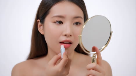woman applying lip balm or lipstick while looking in a mirror