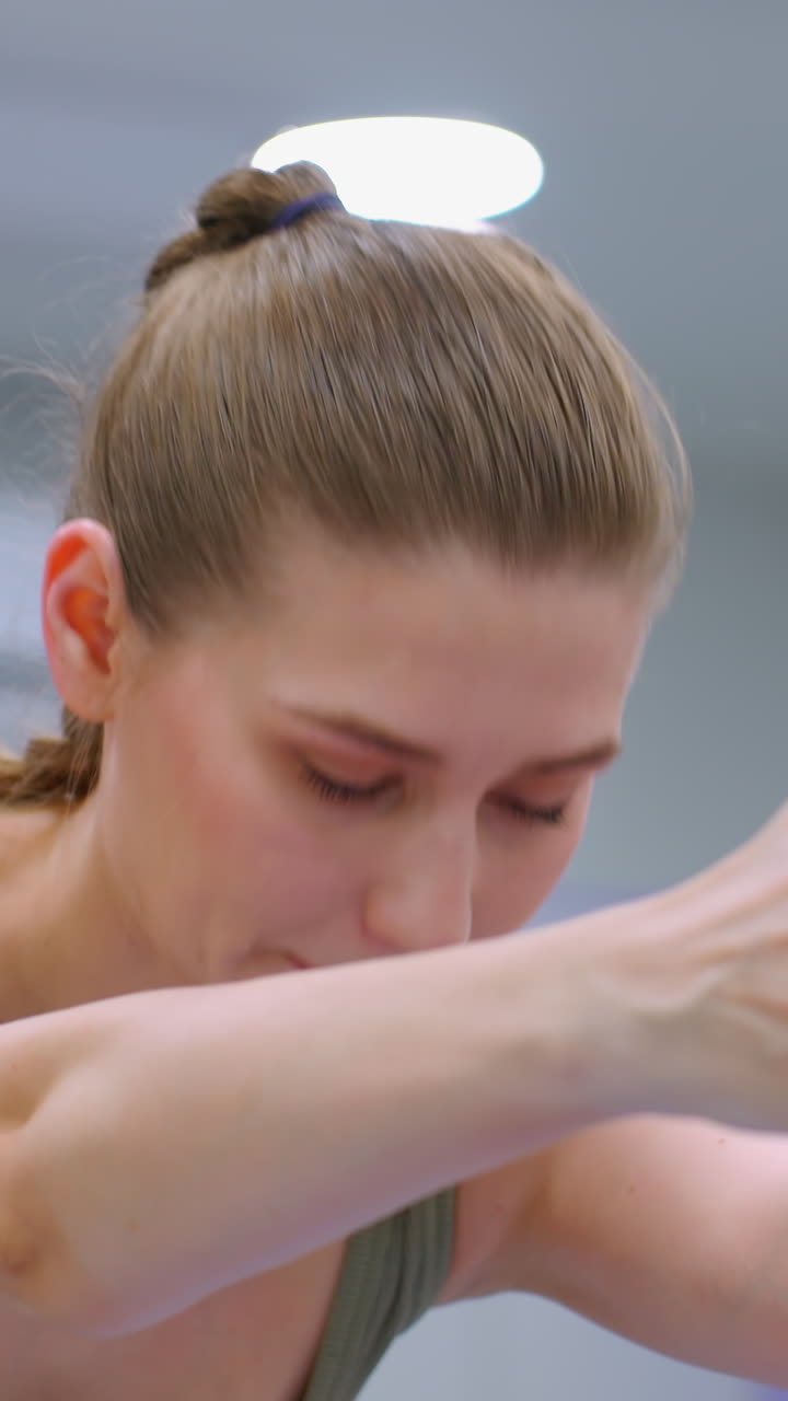 сосредоточенная молодая женщина выполняет приседание, протягивая руки вперед в ярко освещенном тренажерном зале, освещенном потолочными огнями, с решительным выражением лица и сильной позой