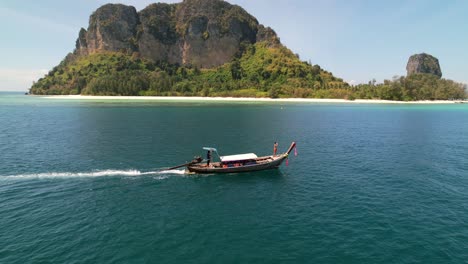 aerial-drone-parallel-with-a-tourist-at-the-front-of-a-thai-longtail-boat-motoring-through-the-blue-andaman-sea-on-a-sunny-morning-around-the-islands-of-Krabi-Thailand-with-Ko-Poda-in-the-distance