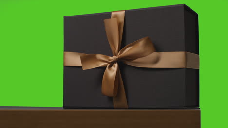 close up of gift wrapped present decorated with ribbon on table shot against green screen 1