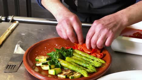 Cook-adds-roasted-peppers-to-an-asparagus,-zucchini,-spinach-and-mushrooms-salad