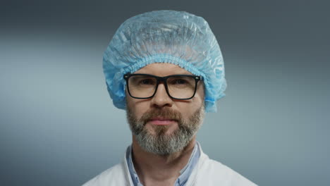 Retrato-Del-Apuesto-Médico-De-Pelo-Gris-Con-Gafas,-Sombrero-Azul-Y-Barba-Sonriendo-Alegremente-A-La-Cámara