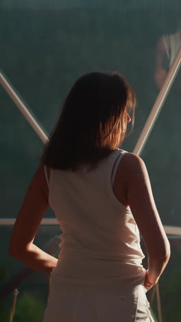 mujer mira en la ventana del espejo por la noche glamping. turista pasa las vacaciones en el campamento de lujo ecológico por la noche. dama reflejada por la pared de vidrio