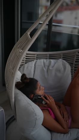 mujer joven relajándose en una silla colgante en el balcón