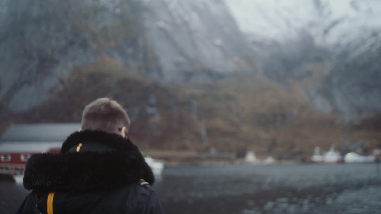 Uomo contempla la vista di un villaggio di pescatori sul mare, Reine, Lofoten, Norvegia