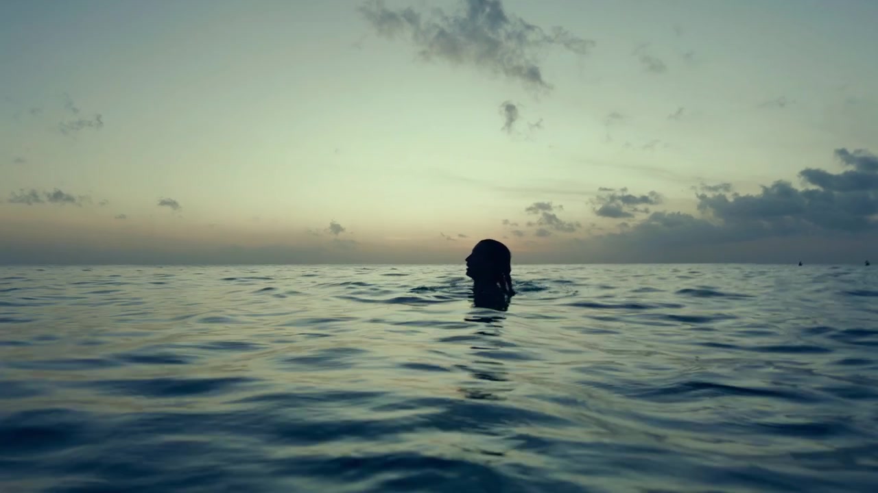 Quiet evening at sea with a solitary man swimming toward the horizon.