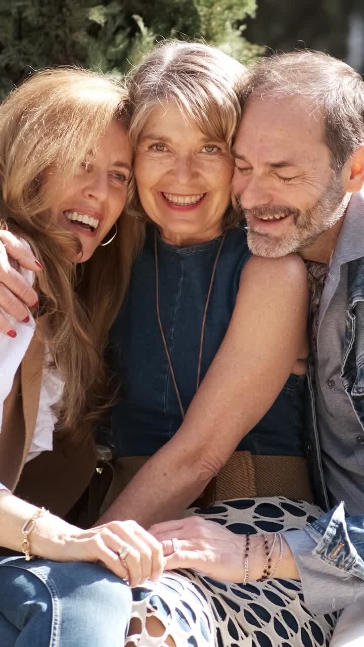 Happy mature friends hugging in park. Vertical footage