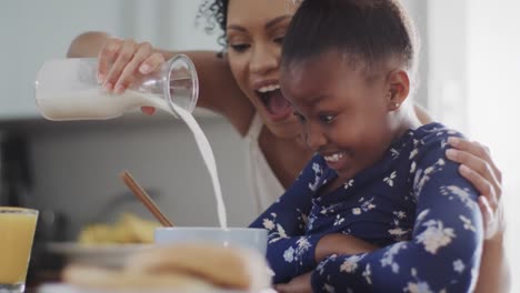 happy african american mother and daughter eating breakfast in kitchen, slow motion