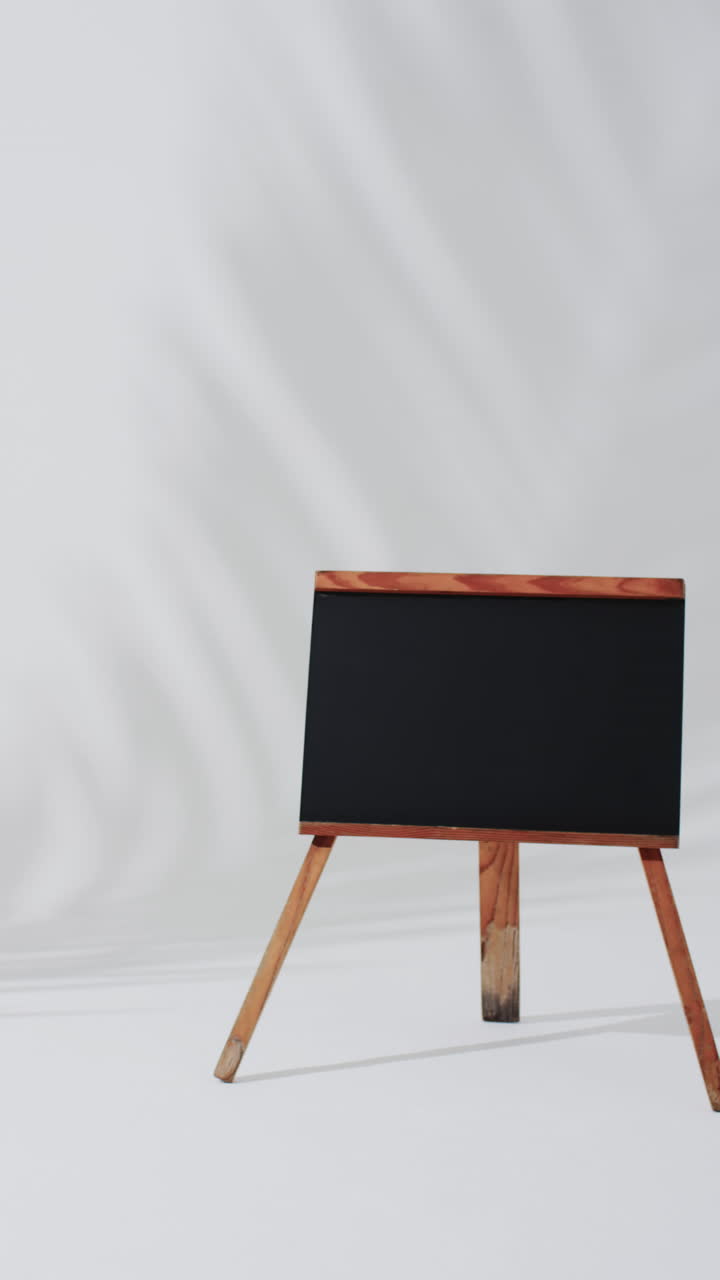 Vertical video of blackboard sign on wooden stand with copy space on white background