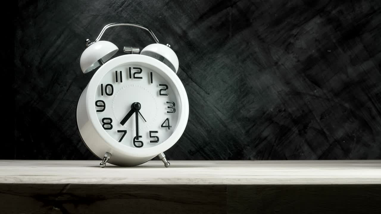 Time lapse of a white vintage alarm clock on wood table with the dark background, time start 07.30 run fast to 07.45