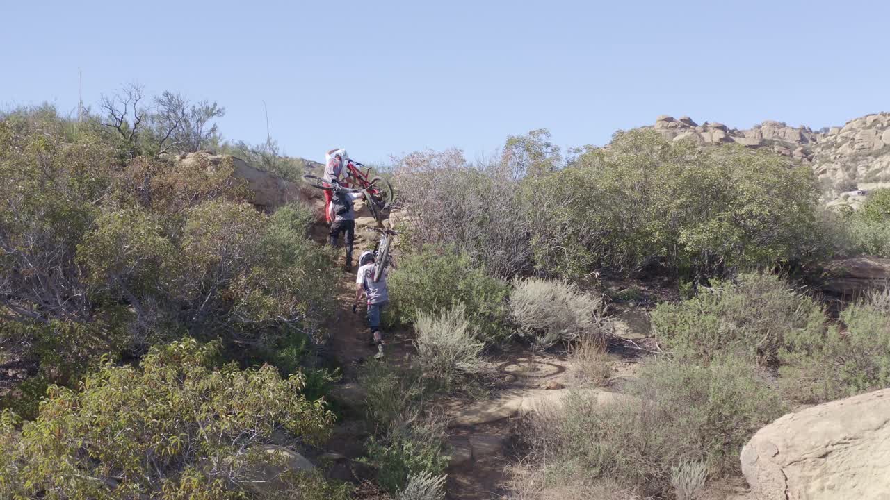 Bikers carrying bikes walking up cliff to jump