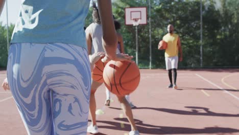 feliz equipo de baloncesto femenino diverso entrenando con un entrenador masculino en una cancha soleada, en cámara lenta