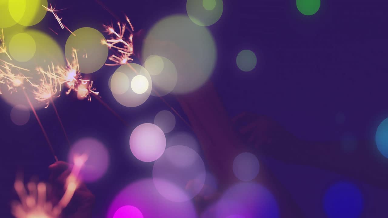 Animation af farverige lyspletter over hænder, der holder nytårsstjernekastere mod nattehimlen