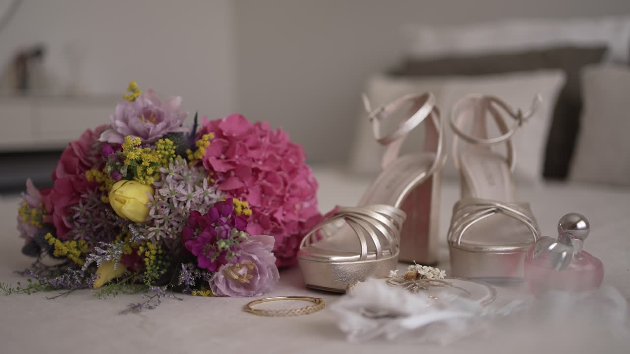 Wedding bouquet, gold high heels, jewelry, and perfume elegantly arranged on a bed