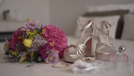wedding bouquet, gold high heels, jewelry, and perfume elegantly arranged on a bed