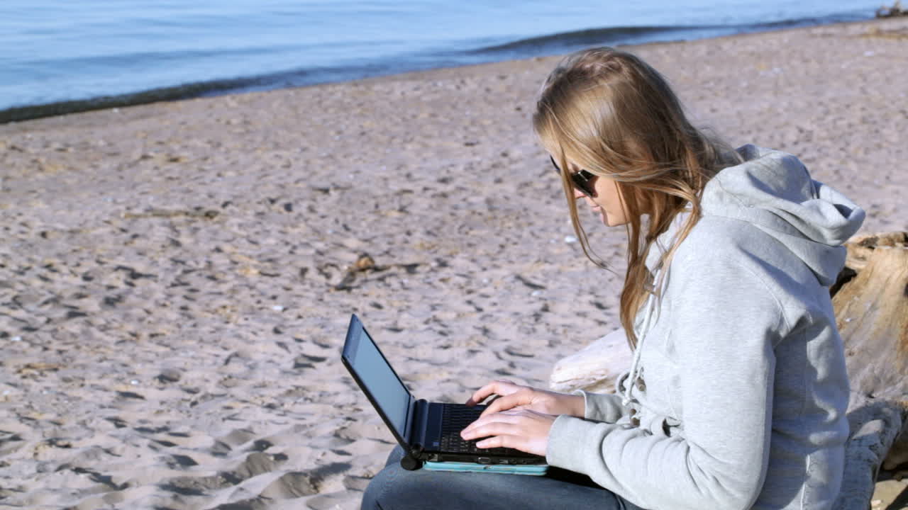 mujer con gafas de sol usando una computadora portátil en la playa