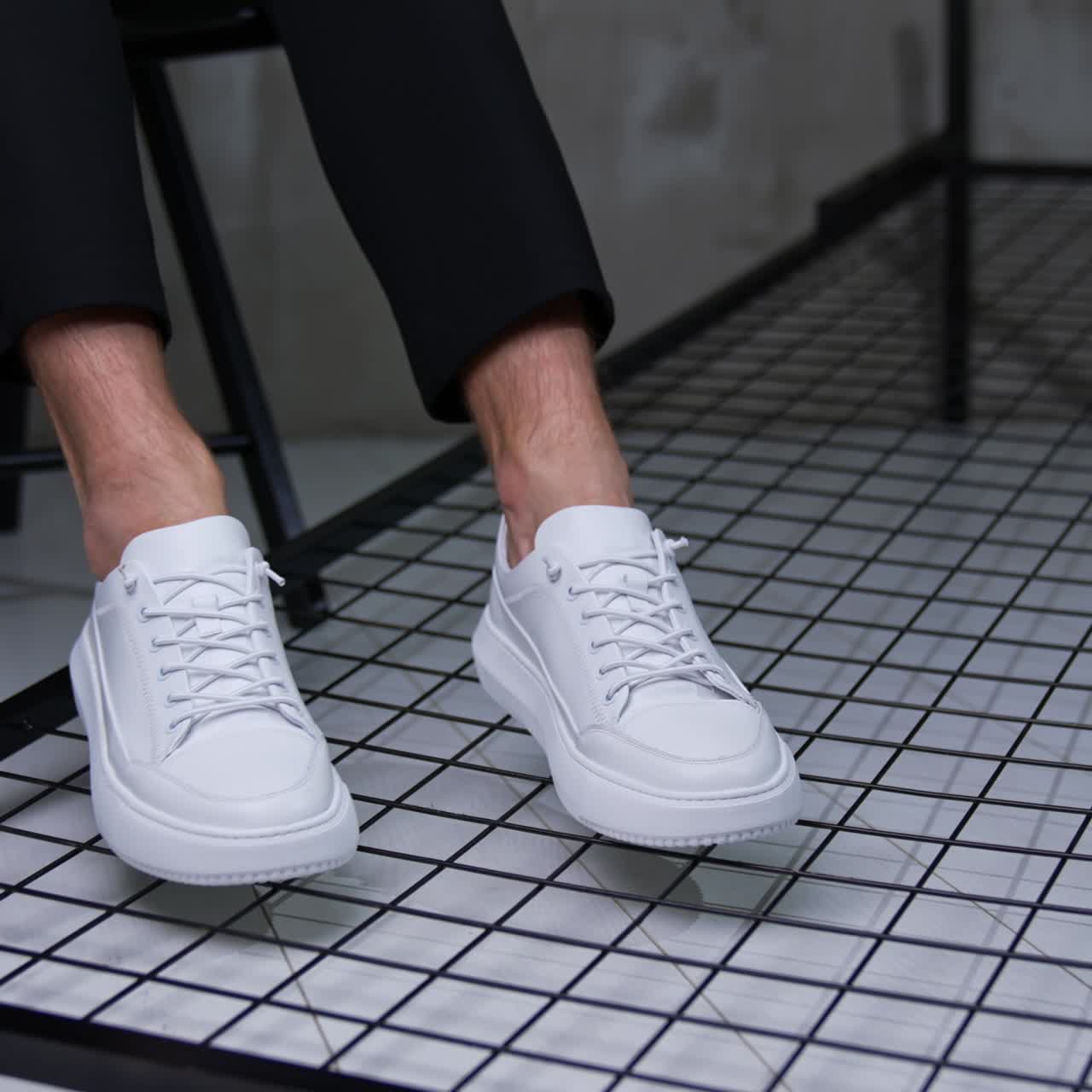 Modern convenient white sport shoes. Male model sits on chair keeping his feet in stylish sneakers close to camera