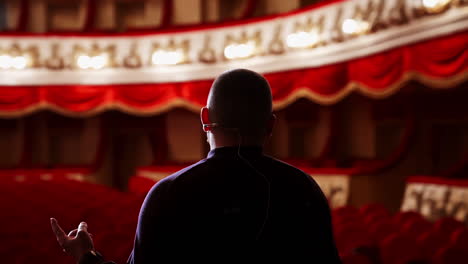 actor rehearsing in front of empty auditorium. back view of a man on stage against spotlight in the theater. male performer speaking on scene. close-up.