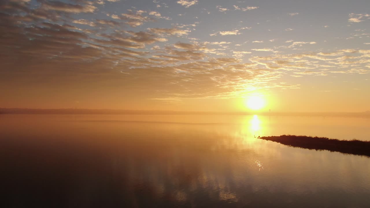 Il sole sorge e si riflette su un lago nebbioso con un cielo drammatico sopra, spazio per il testo