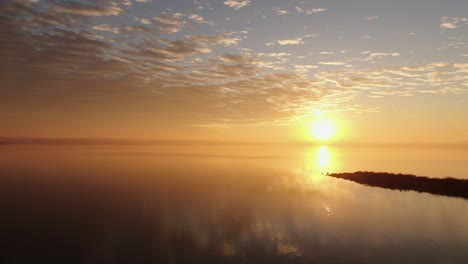 Sun-rises-and-reflects-bouncing-off-of-misty-lake-with-dramatic-sky-above,-space-for-text