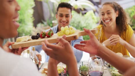 grupo de diversos amigos masculinos y femeninos sosteniendo un tablero de frutas en una cena en el patio