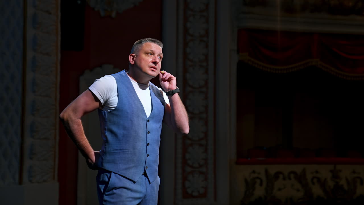 Host in grey suit on stage. Male actor starts his performance in the theater. Portrait of a comedian standing on stage and talking.