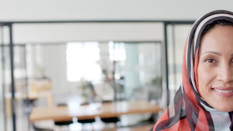 Portrait-of-happy-biracial-businesswoman-with-hijab-in-office-in-slow-motion