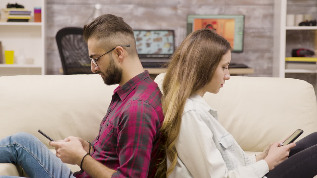 Couple sitting back to back on a couch using smartphones