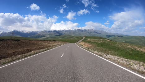 point of view driving a car on a road. mount elbrus is visible in the background.