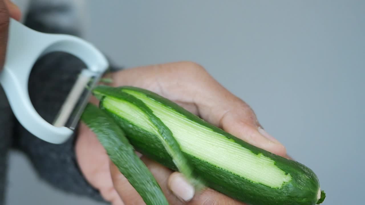 A person peeling a green vegetable with a peeler