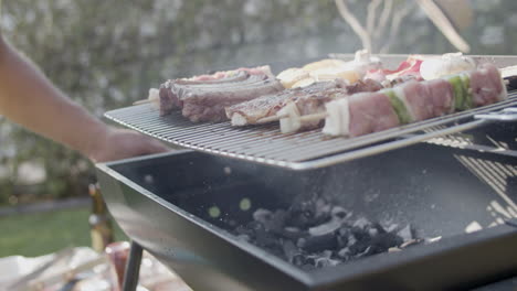 parrilla de barbacoa con carne y hombre agitando y soplando carbón