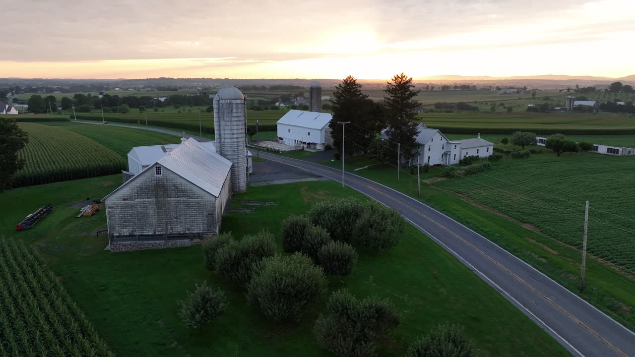 Rustic American farmstead and agricultural fields at golden sunrise. Aerial approaching shot. Intersection road in rural district of town. Peaceful landscape in Pennsylvania, USA