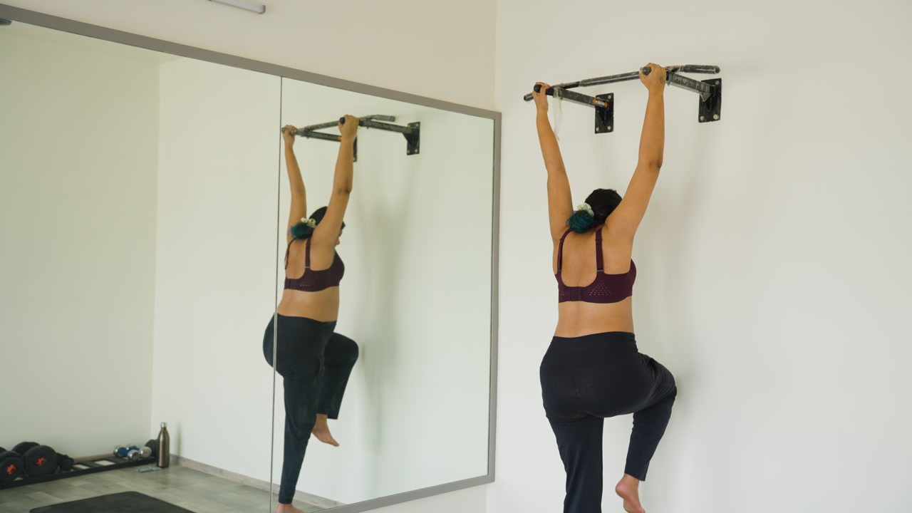 Indian female hanging from gym bars hip mobility in third trimester health care workout routine