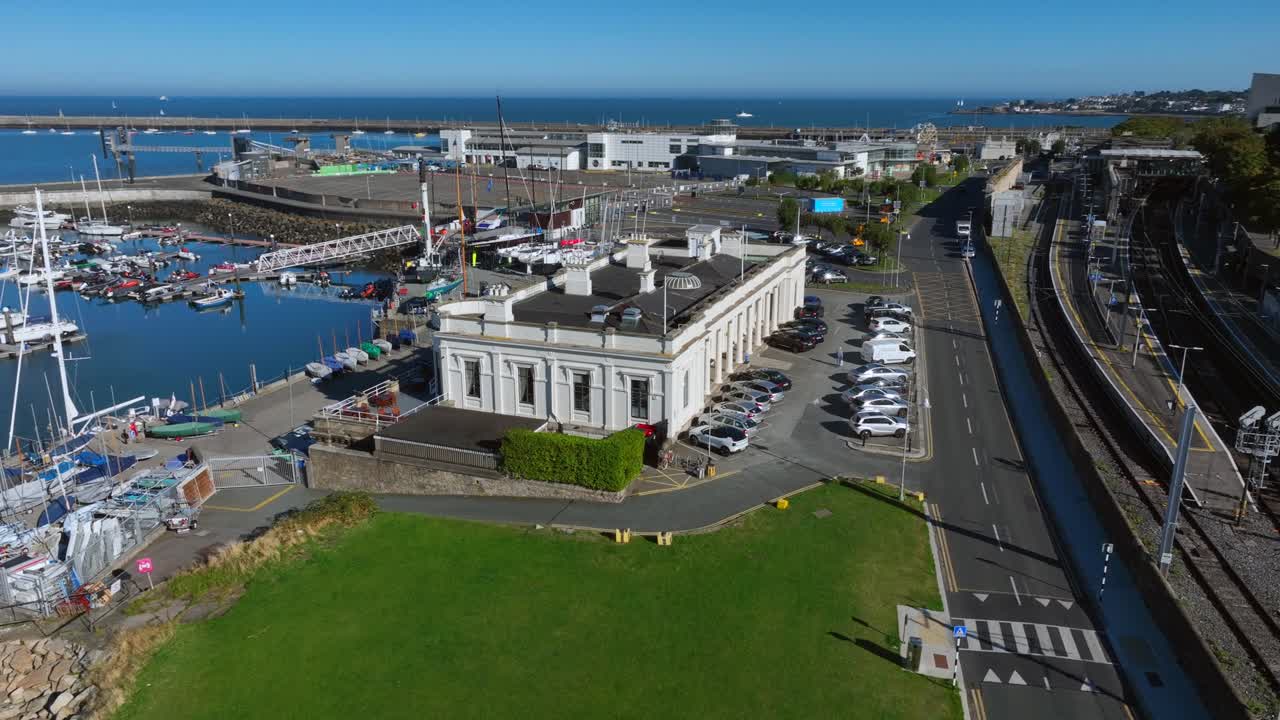 Royal Irish Yacht Club, Dún Laoghaire, County Dublin, Ireland, September 2024. Drone orbits counter clockwise above a lawn revealing the front facade of the building with the Marina behind.