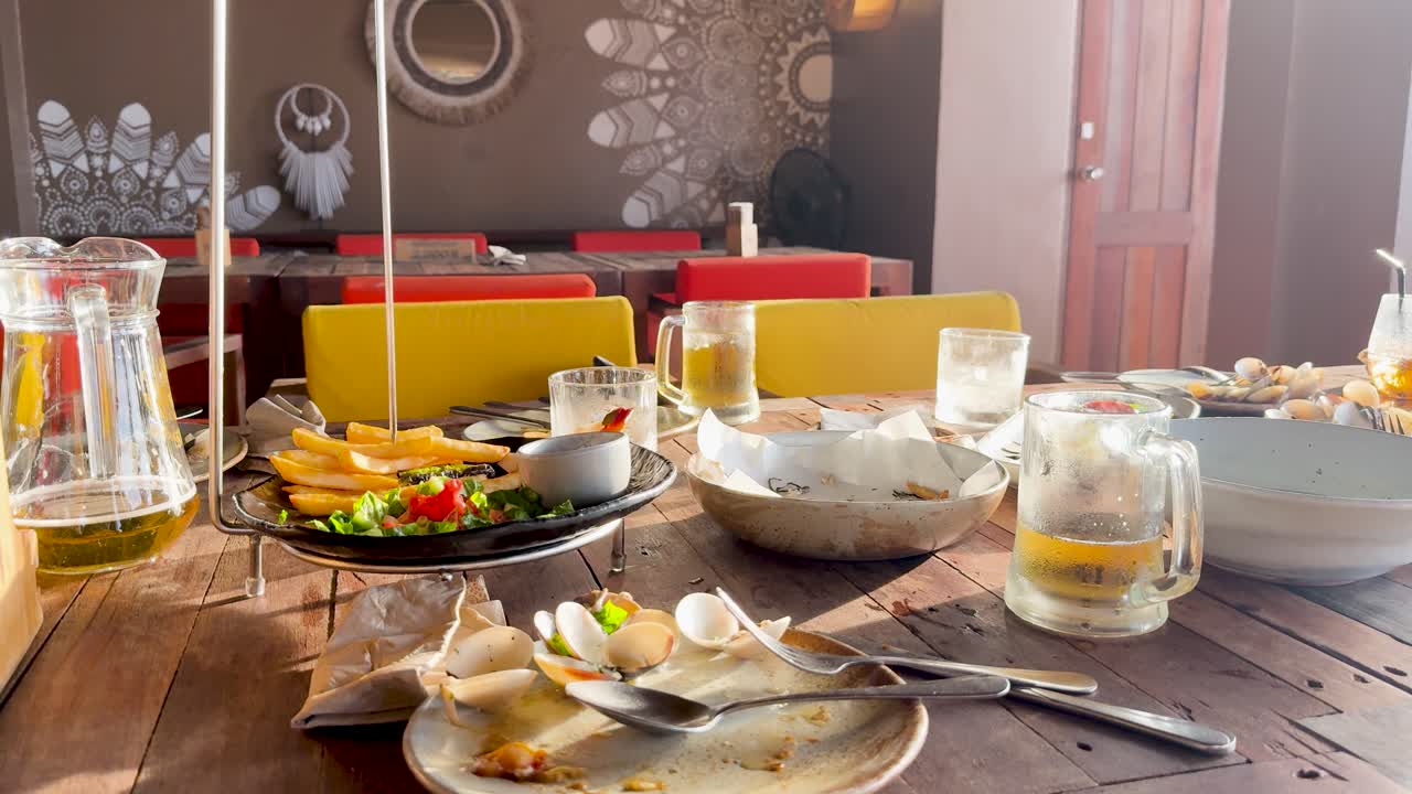 A vibrant table setting with beer, salad, fries, and clams under warm natural lighting at a beach club