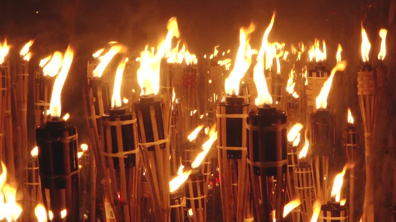 Close-up of a single lit bamboo torch with many others glowing in the blurred background, creating a warm and intense flame-filled atmosphere